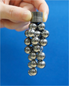 今回開発した重希土類元素を含まない高性能焼結磁石（Sm-Fe-N系） 高性能焼結磁石を2段重ねにしたものに、鉄球30個が磁着している